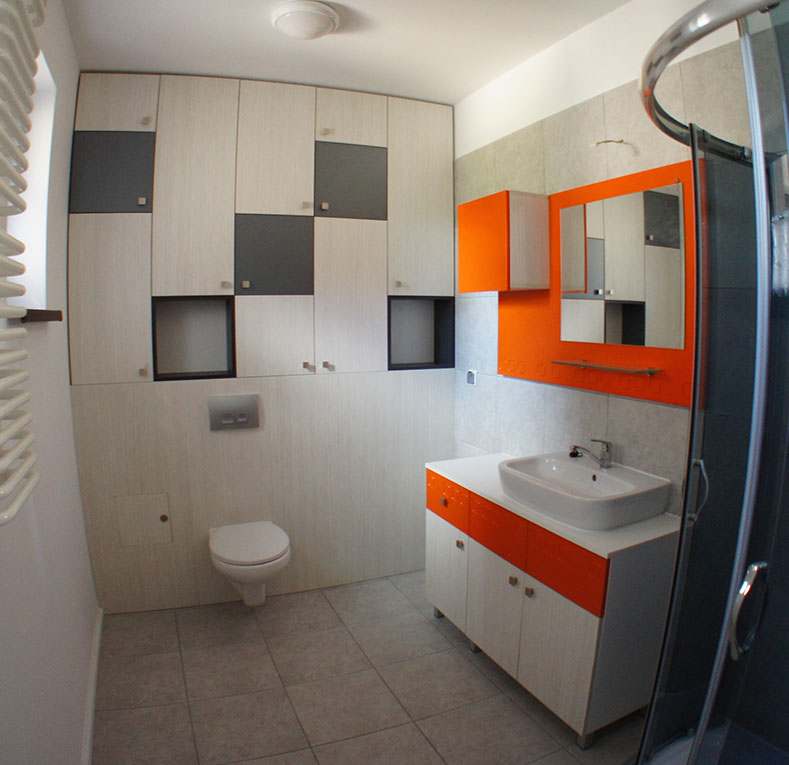 Łazienka z pomarańczowymi akcentami. Nowoczesne wnętrze z wbudowanymi w ścianę licznymi szafkami wspomagającymi użyteczność wnętrza