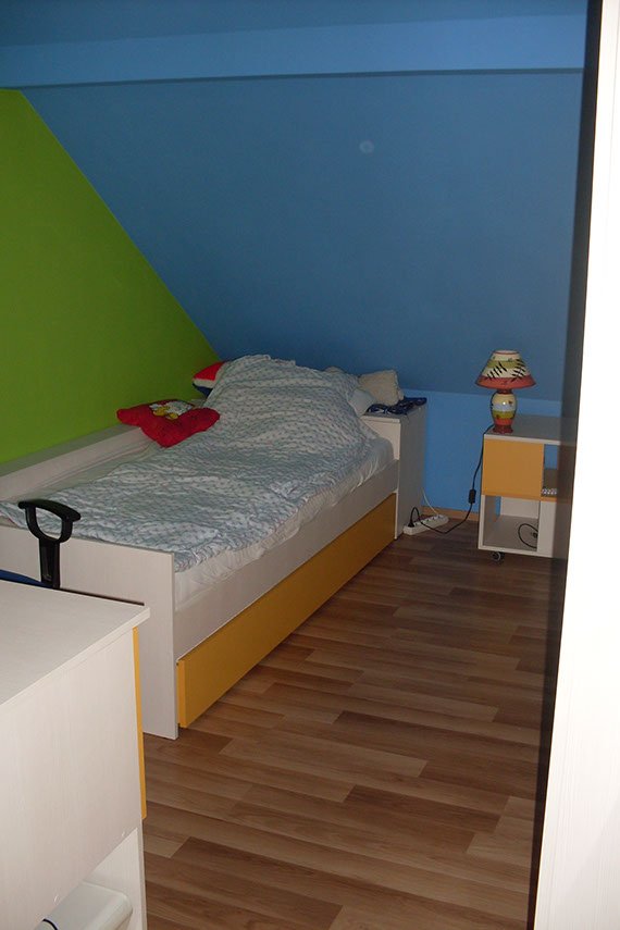 Widok pokoju dziecka na poddaszu z łóżkiem w rogu, gdzie znajduje się spad dachu